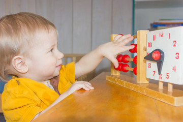 A child plays with a toy clock. The boy studies time, hours. A child learns to count.