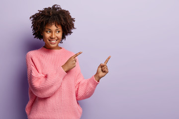 Studio shot of attractive young female with curly hair, toothy smile, healthy dark skin, points...