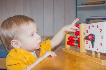 A child plays with a toy clock. The boy studies time, hours. A child learns to count.