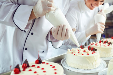 Two pastry chefs decorate a cake from a bag in a pastry shop - obrazy, fototapety, plakaty