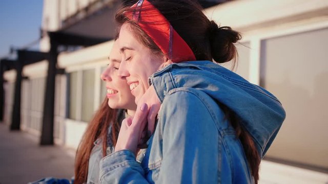 Two young lovely sisters hug tightly each other and hold the hand, enjoying sea side view en Europe, feel tenderness and trust, friends for ages, dressed in jeans jacket and headband,
