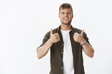 Nice work, you cool. Portrait of impressed and pleased male friend with charming smile showing thumbs-up in cheer and support, totally agree and satisfied with excellent choice over grey background