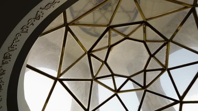 A panning, low angle, extreme close up shot of the ceiling of the tower, made out of glass and golden metal.