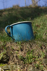 Old enamel metal battered mug grass garden with sky background