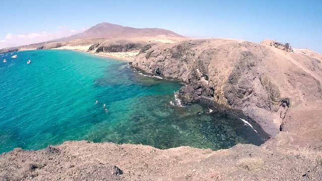 Pan at playas papagayos in lanzarote showing people swimming and boats in the ocean.