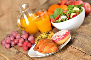 Fototapeta na wymiar Croissant and donuts, orange juice and fresh salad - breakfast on wooden table