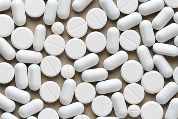 different types of white pills scattered on a beige surface as background