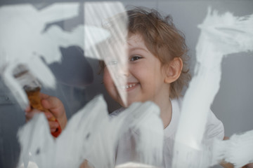 The child draws the sun with white paint on a glass Board. Simulated screen. Happy child