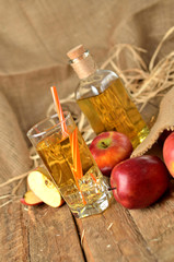 Juice from fresh apples, straw, ice and bottle in background on wooden boards vertical photo