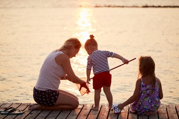 Happy kids playing with mother on the beach at the sunrise time with fishing net. Family and friendships concept. Summer time
