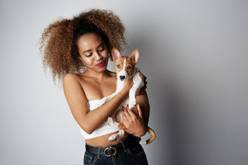 Pretty young black american african girl embracing puppy on white background. Studio portrait of white appealing female chilling with dog on white background
