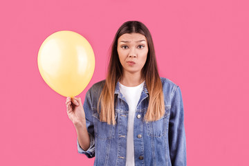 Unhappy young girl holding yellow balloon with smiling face isolated on pink background