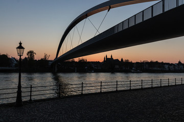 Obraz premium Sunset in downtown Maastricht seen from the riverside with a view on the historic skyline with the churches and hoge brug (high bridge)
