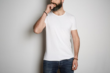 Young brutal tattooed bearded guy poses in blue jeans and blank white t-shirt premium summer cotton, on white background