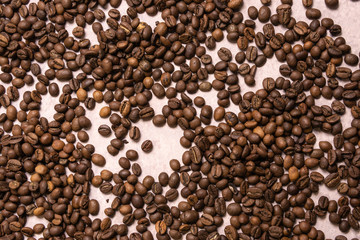 Roasted coffee beans in bulk on a light pink background