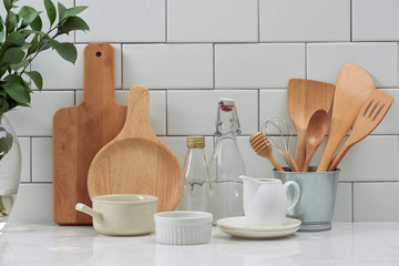 Simple rustic kitchenware against white wooden wall: rough ceramic pot with wooden cooking utensil...