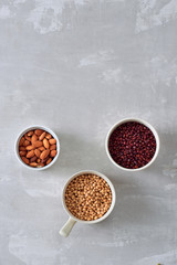 various dried beans with kitchen utensils on gray table, top view