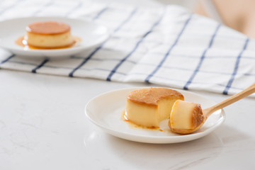 Woman's hand cutting homemade caramel custard pudding on white plate. Over white table with napkin.