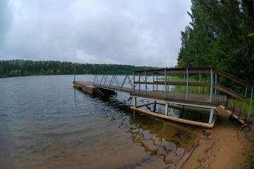 Boat pier on a forest lake on a rainy summer day