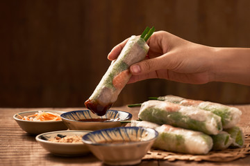 Hand dipping vegetarian rice paper rolls into the soy sauce - obrazy, fototapety, plakaty