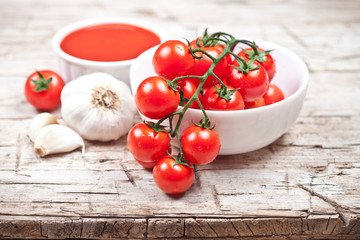 Fresh tomatoes in white bowl, sauce and raw garlic on rustic wooden table.