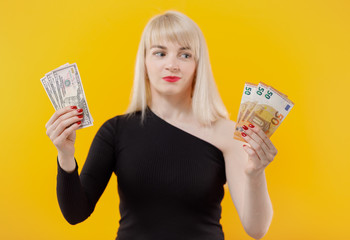 Young blonde girl holding money banknotes isolated over yellow background.