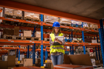 Warehouse female worker checking inventory in distribution warehouse. Smiling woman holding checklist.