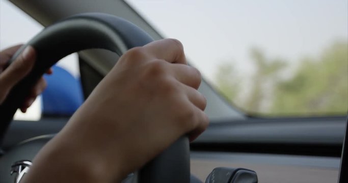 Woman driving car - close up on hands turning steering wheel