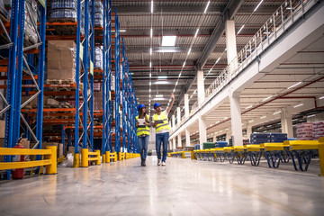 Distribution warehouse interior with workers wearing hardhats and reflective jackets walking in...
