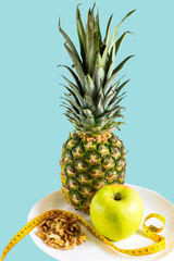Diet, healthy food, vitamins, fitness diet food concept. Pineapple, apple, nuts on a plate on a blue background