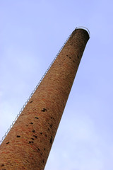 Fototapeta premium Old weathered tall industrial factory chimney, red grungy brick smokestack perspective