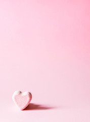 Pink small bath bomb in the shape of heart on soft pastel background.