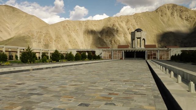 A panning, long shot of a paved pathway leading to the entrance to a mausoleum.