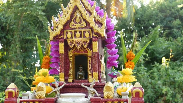 Wooden miniature guardian spirit house. Small buddhist temple shrine, colorful flower garlands. San phra phum erected to bring fortune. Traditional respect animistic rituals, pray ceremonies.