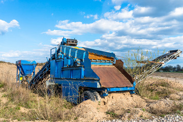 Fototapeta premium Old, mobile screen for gravel and sand in blue color standing on the field, in the background blue sky with clouds.