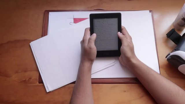 Top view. Male hand reading and turning pages on a ebook reader. from wooden desk. Man switch off an ebook reader. Vr headset on left side. 3d experience with a vr headset