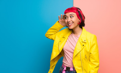 Young woman with yellow jacket listening to something by putting hand on the ear