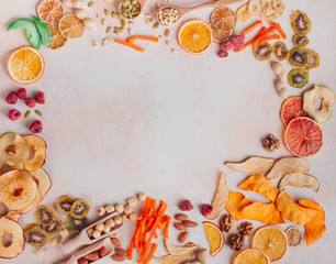 Frame of dried fruit and vegetable chips, candied pumpkin slices, nuts and seeds on beige concrete background