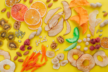 Dried fruit and vegetable chips, candied pumpkin slices, nuts and seeds on yellow background
