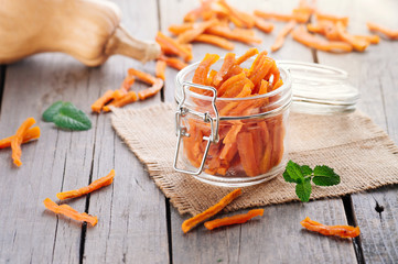 Homemade candied pumpkin slices in glass jar on rustic wooden background