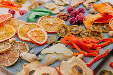 Mixed dried fruit and vegetable chips, candied pumpkin slices, nuts and seeds on blue wooden board