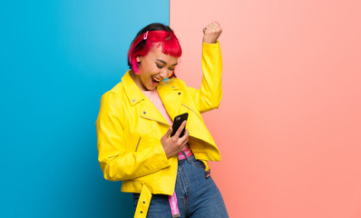 Young woman with yellow jacket celebrating a victory with a mobile