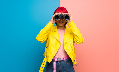 Young woman with yellow jacket and looking in the distance with binoculars