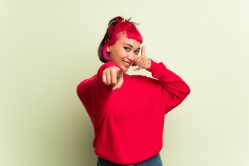 Young woman with red sweater making phone gesture and pointing front
