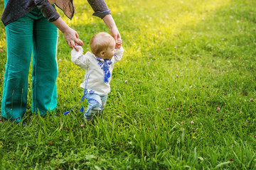 Fototapeta premium The baby learns to walk hand in hand with his mother, the baby walks on the grass.