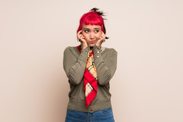 Young woman with pink hair over yellow wall frustrated and covering ears