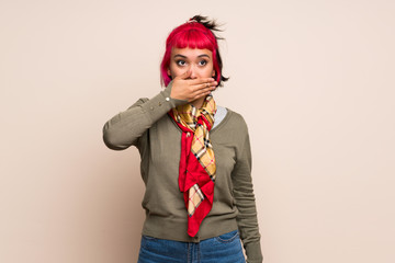 Young woman with pink hair over yellow wall covering mouth with hands