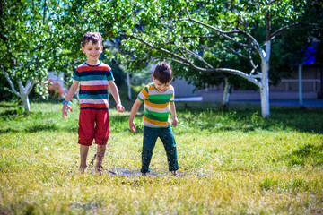 Fototapeta premium Little boy and his brother play in summer park. Children with colorful clothes jump in puddle and mud in the garden.