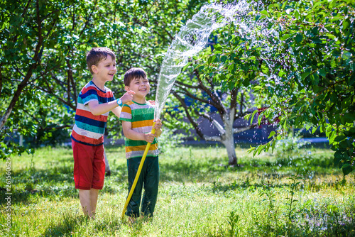Cute Little Boy Watering Plants With Hose In The Garden Cute Little Boy Watering Plants With Hose In The Garden