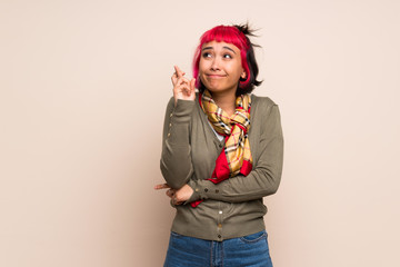 Young woman with pink hair over yellow wall with fingers crossing and wishing the best